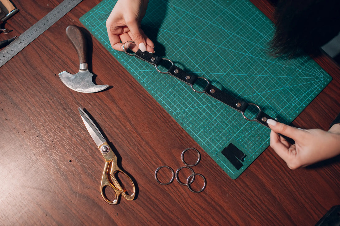 Fabrication artisanale d'un collier pour chien en cuir noir avec anneaux métalliques sur planche de découpe verte